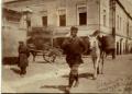 Man walking through a cobblestone street in Tiflis leading a donkey carrying large water containers, with buildings in the background.