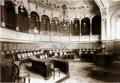 Black and white 19th-century interior photograph of the Town Council meeting hall in Tiflis, showing curved desks, tiered seating, chandeliers, and ornate architectural detailing.