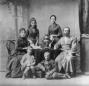 Studio portrait of the Georgian aristocratic Gedevanishvili family seated around a table with a samovar, including three women, one man in traditional chokha, and three children.
