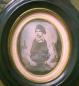 Daguerreotype portrait of young child in dark clothing with bow tie, in ornate oval frame.