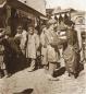 Photograph showing several men standing and interacting in a street area of the Tiflis bazaar, late 19th century.