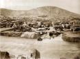 Panoramic view of Tbilisi across the Mtkvari River with dense historic buildings and surrounding hills.