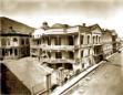 Two-storey 19th-century building with wraparound balconies and arched windows on a street in Tbilisi.