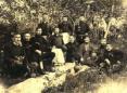 Group of men seated and standing outdoors in a wooded area