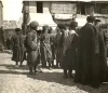 Street scene in Tiflis showing several men with two-wheeled handcarts and people gathered along a cobbled street.
