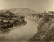 Panoramic view of Tiflis with the Mtkvari River in the foreground and hillside buildings rising above the city.