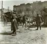 Municipal workers cleaning or repairing a street with tramway tracks in Tiflis, with carts and tools visible and a large building in the background.