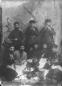 Seven Georgian men in traditional clothing posing indoors during a feast, with musical instruments and food placed on the floor.