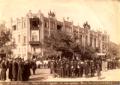 Large crowd gathered along a decorated boulevard in Tiflis during an imperial visit, with buildings adorned with banners and flags.
