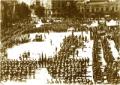 Gelatin silver photograph showing a large military formation and assembled crowd in a city square surrounded by historic buildings.