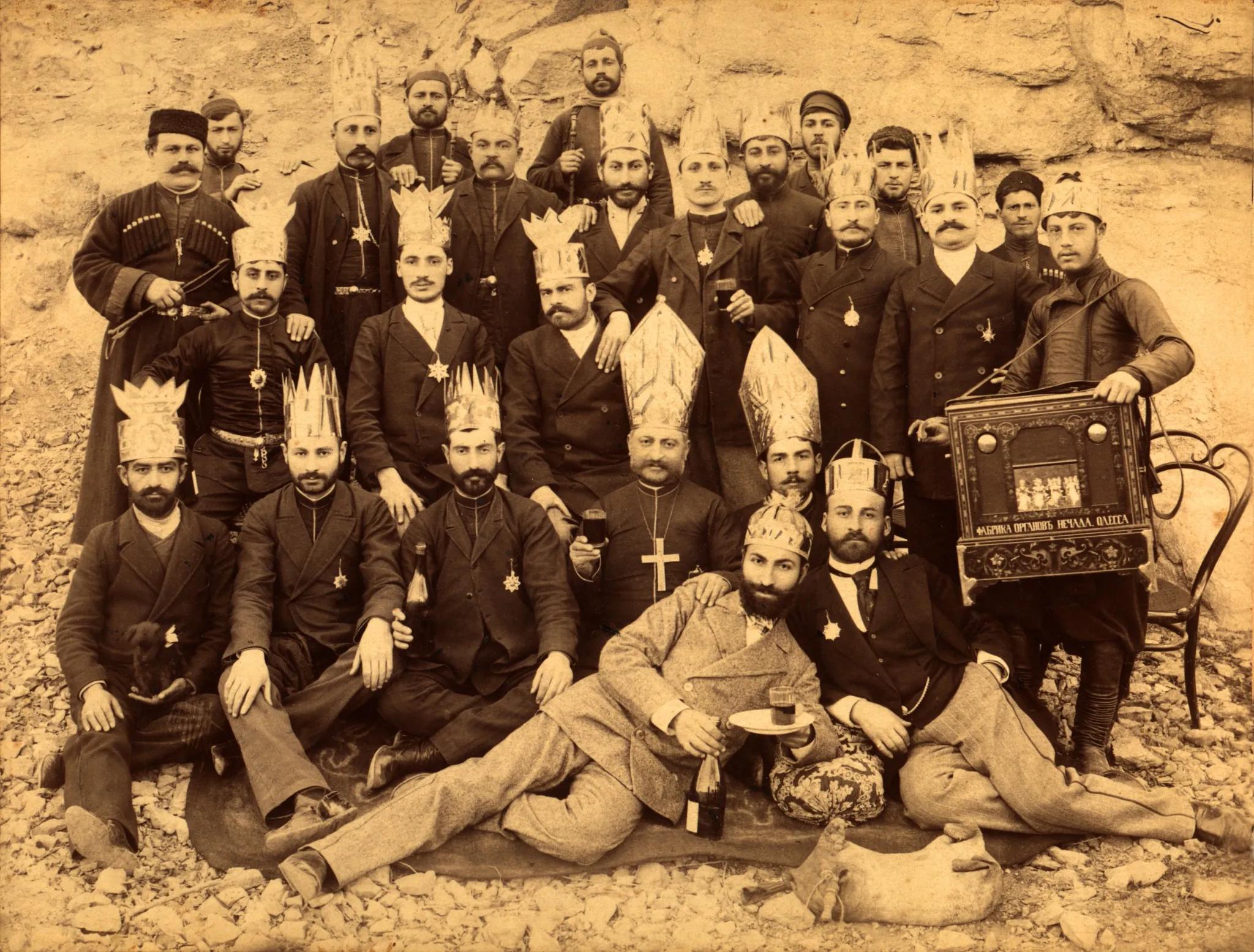 Group of men gathered outdoors during a public festival, some wearing traditional attire and ceremonial headwear.