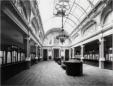 Large interior operating hall of the State Bank Office with glass ceiling, chandeliers, service counters, and patterned floor.