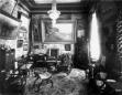 Black-and-white photograph of an ornate early 20th-century interior with paintings, carved furniture, carpets, and a chandelier in David Sarajishvili’s house.