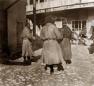 Photograph showing three men standing in a cobbled courtyard area of the Tiflis bazaar with market buildings and carts visible in the background.