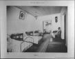 Interior of a hospital room with several beds, tables, and two people inside the Kutaisi Male Gymnasium.