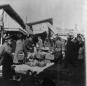 Busy bazaar street in Tiflis with fruit and vegetable vendors selling produce from baskets and stalls while people gather around.