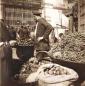 A fruit vendor standing beside baskets filled with grapes and other produce at a bazaar stall in Tiflis.