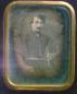 Daguerreotype portrait of man in dark formal suit with mustache, in brass frame.