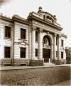 Monumental stone bank building with columns and arched central entrance on a cobblestone street in Tbilisi.