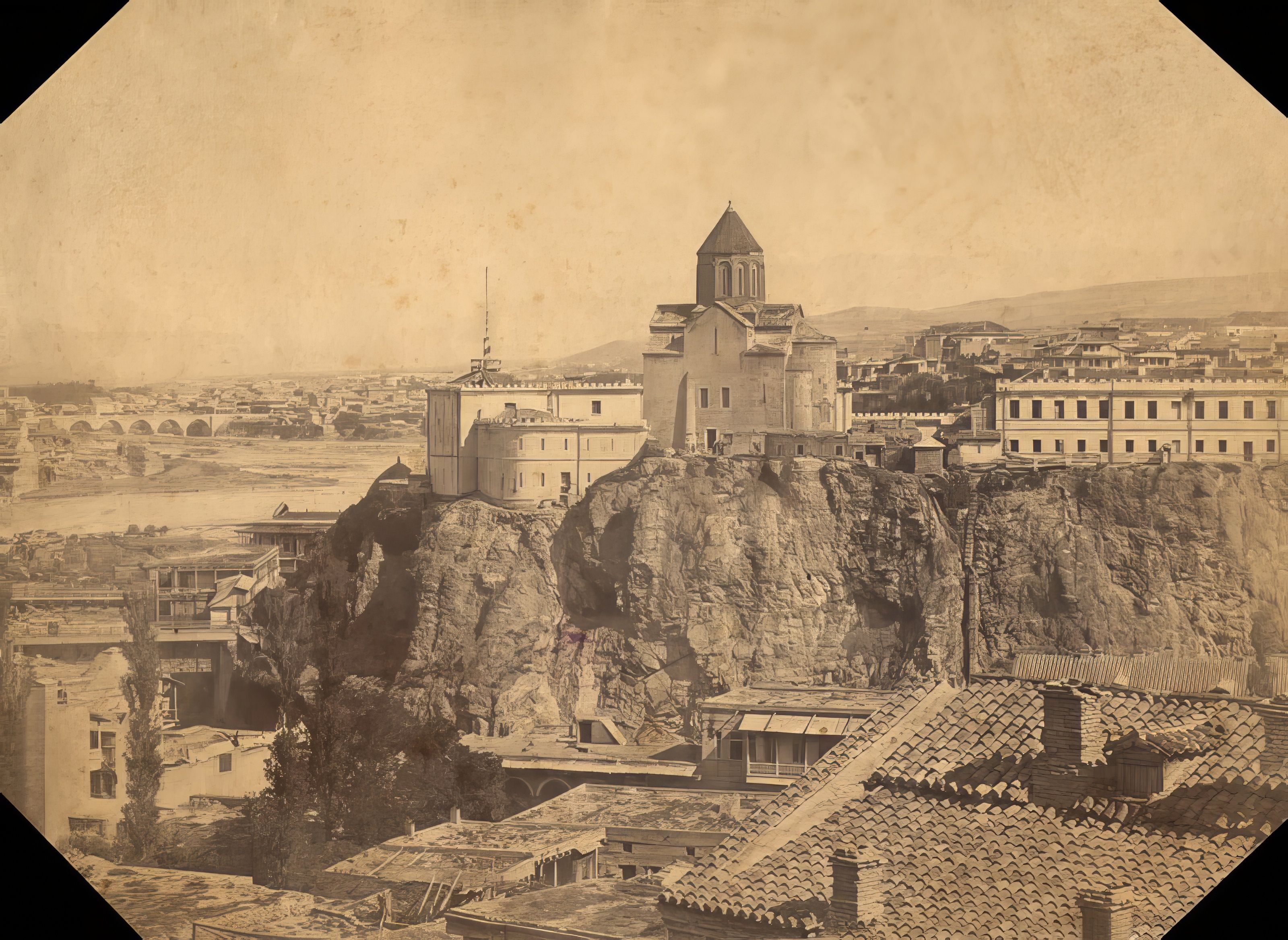 Black and white photograph showing multi-story wooden houses with balconies built on a hillside overlooking a gorge with vegetation.