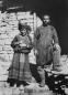 Gelatin silver photograph showing a man and woman in traditional Khevsurian dress standing in front of a stone structure, 1930.