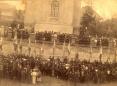 Large crowd gathered outside a church building in Tiflis during a funeral memorial ceremony, with flags arranged in the foreground.