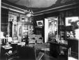 Black-and-white photograph of an ornate early 20th-century interior with paintings, carved furniture, carpets, and a chandelier in David Sarajishvili’s house.