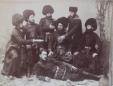 Seven men in traditional Georgian clothing and fur hats pose together, one reclining in front while others stand and sit around him.