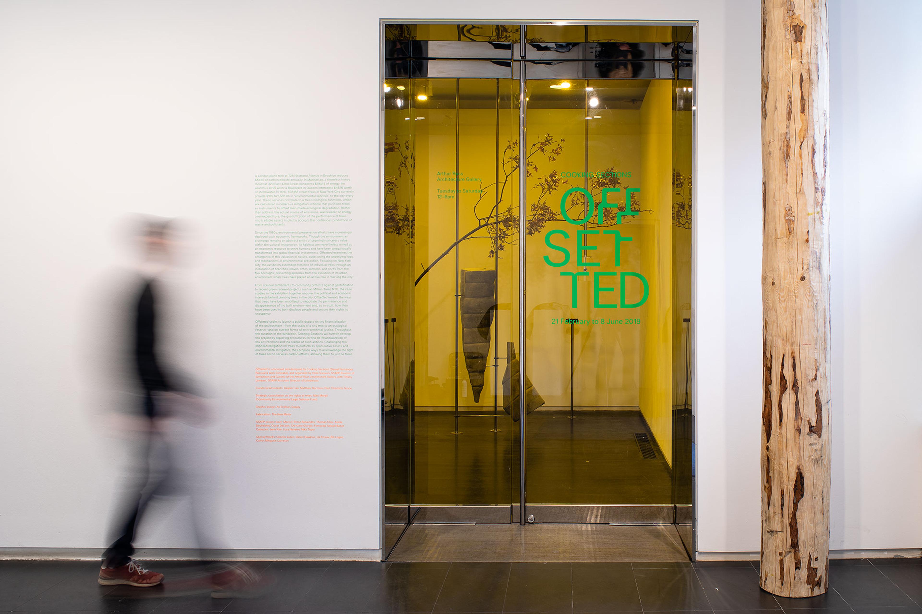 Photograph of interior exhibition vinyl. The title 'Offsetted' in green cut vinyl on glass door to gallery and green interpretation text on a white wall next to the door.