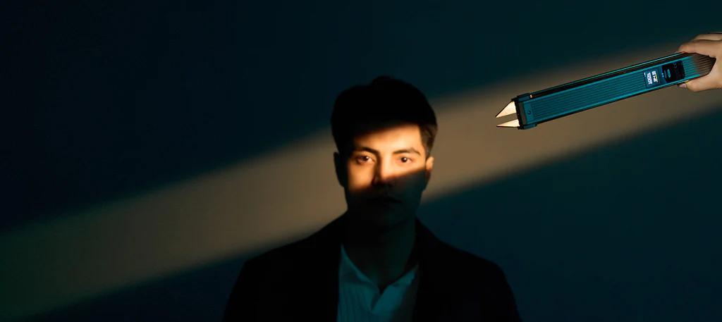 Una mano sujeta una elegante Blade 10, proyectando luz sobre el rostro de un hombre, que está parcialmente envuelto en sombras contra un fondo oscuro.