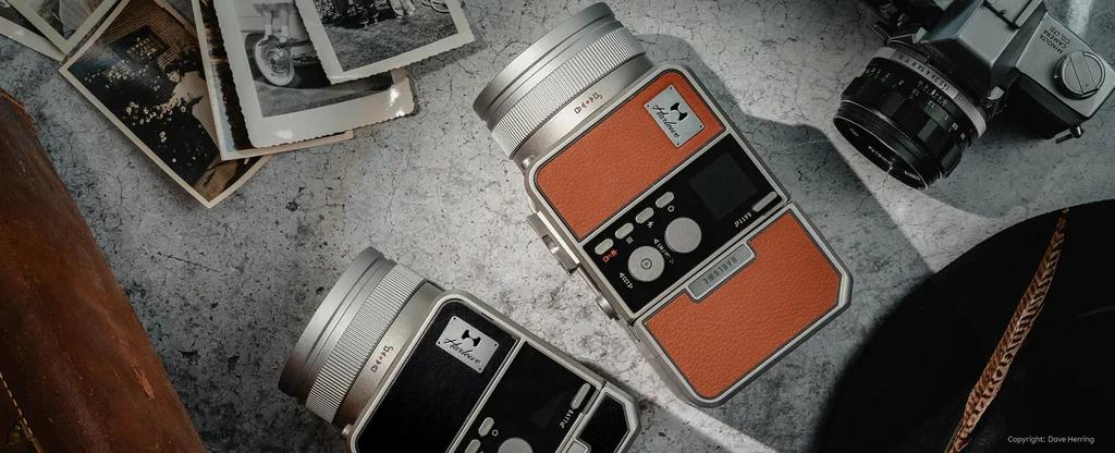 Two vintage-style cameras with orange and silver detailing, surrounded by old photographs and a leather bag.