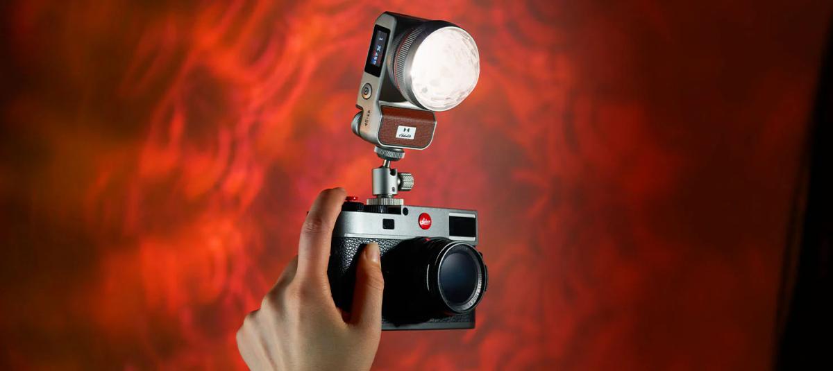 A hand gripping a Hobolite Iris featuring a mounted flash set against a striking red backdrop.