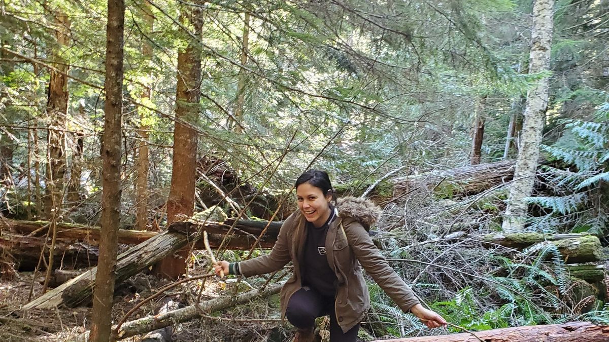 Hillary smiling and posing on a log in the forest of Oregon.