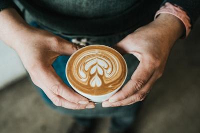 Coffee with leaf pattern in the foam held in 2 hands