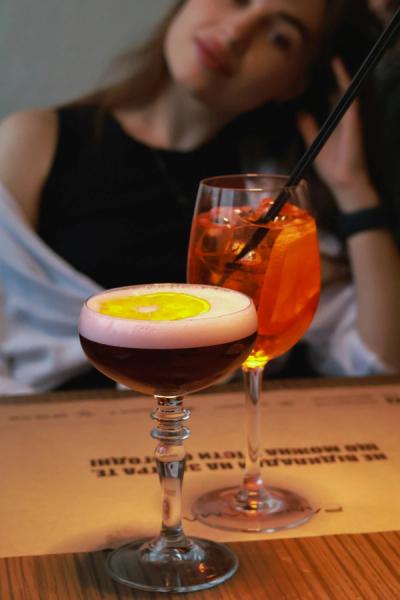 Cocktail and Aperol sprittz on table with a woman seated in the background