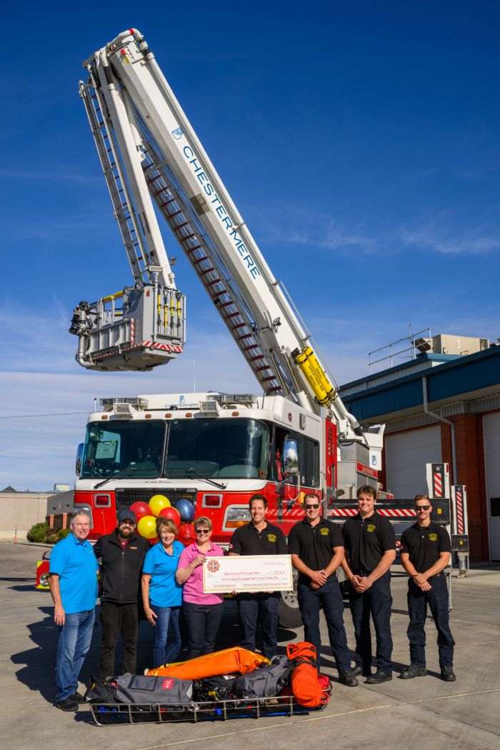 Interior of a Firehouse Subs restaurant featuring a wooden table with red chairs, black hanging lights, and a wall decorated with firefighting-themed artwork and memorabilia.