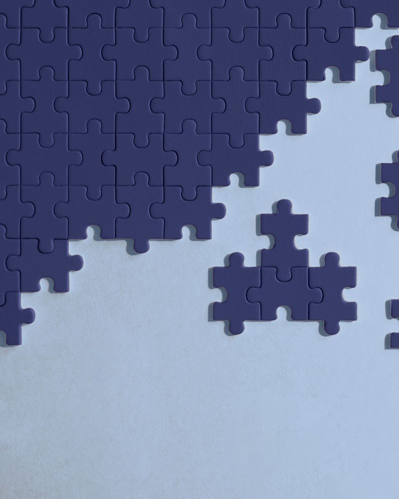 Dark navy puzzle pieces partially assembled on a pale blue background, with several loose pieces scattered nearby.