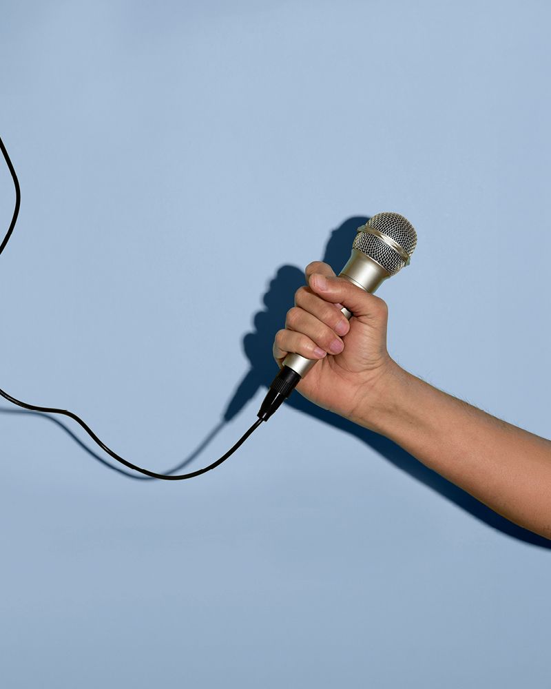 A hand holding a silver microphone with a black cable against a soft blue background.