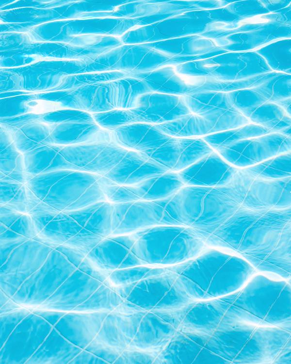 Close-up of bright turquoise pool water with sunlight reflecting off the rippled surface and tiled base.