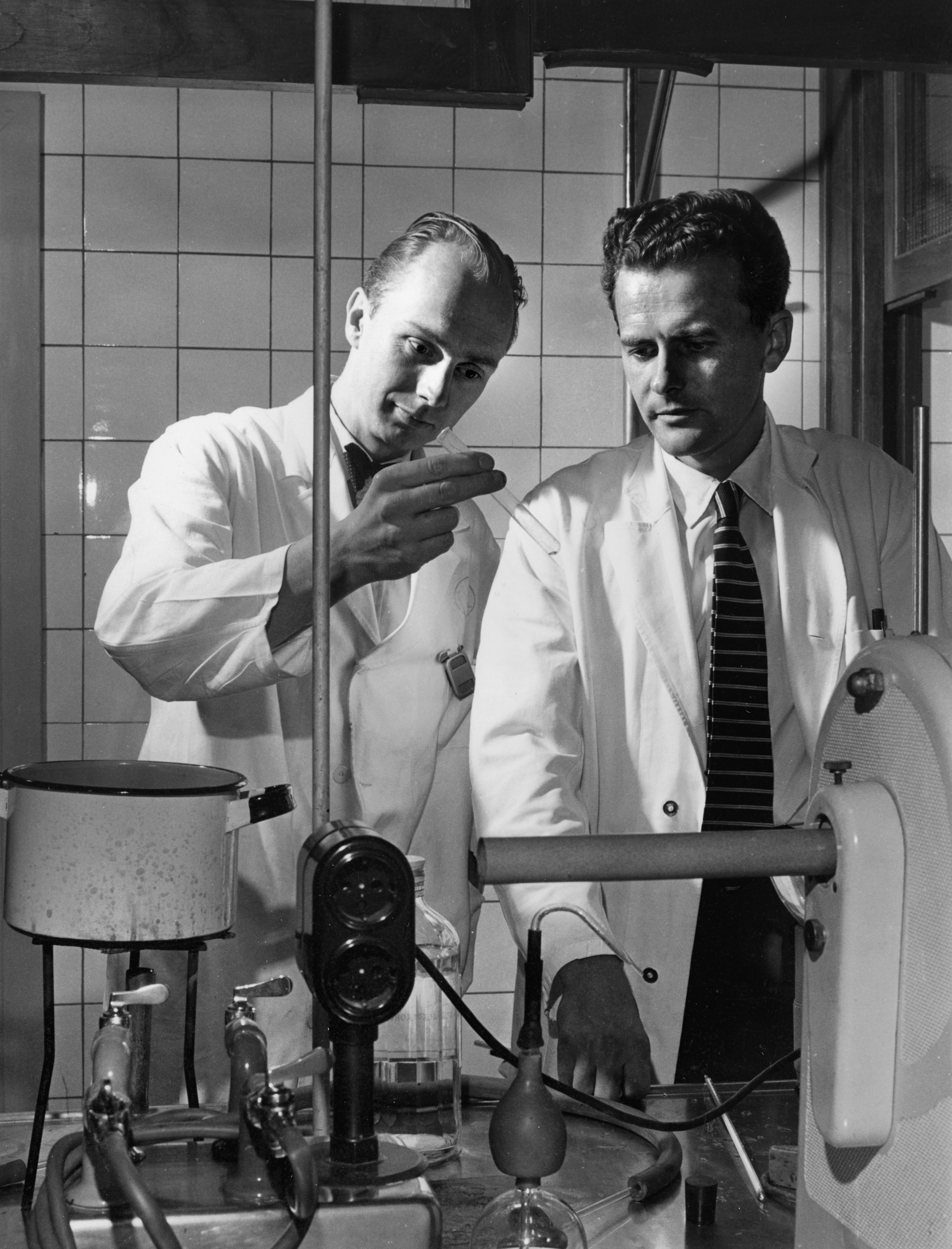 a black and white photo of two men working in a lab