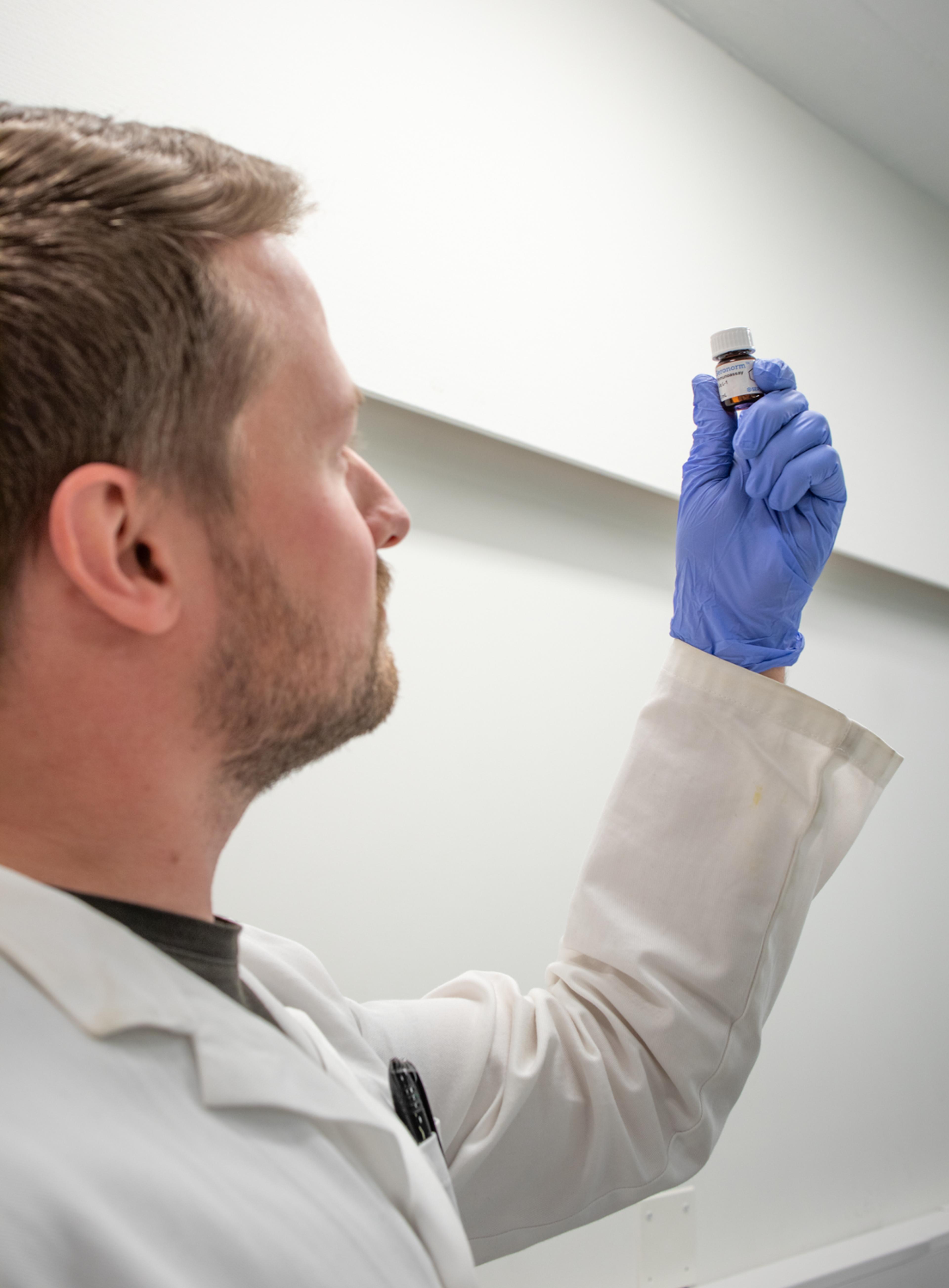 a man in a lab coat and blue gloves is holding a small bottle