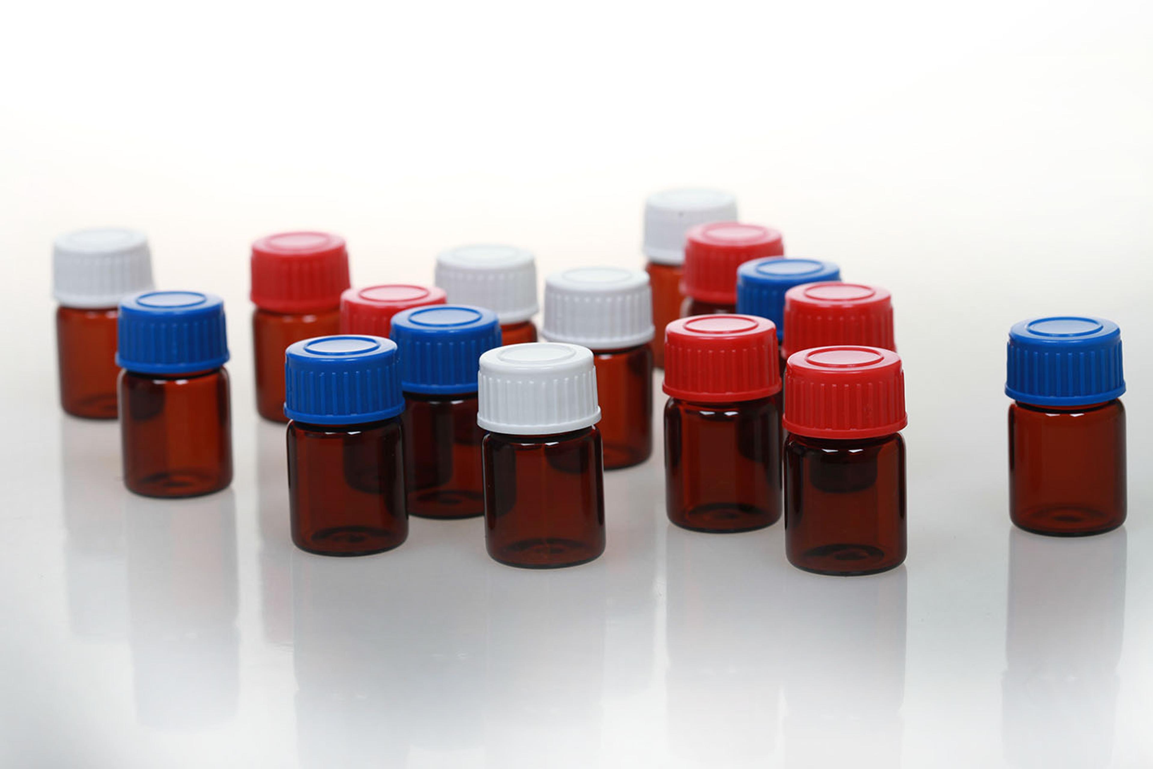 a group of small glass bottles with red , white and blue caps on a white surface . quality control sero trace elements 