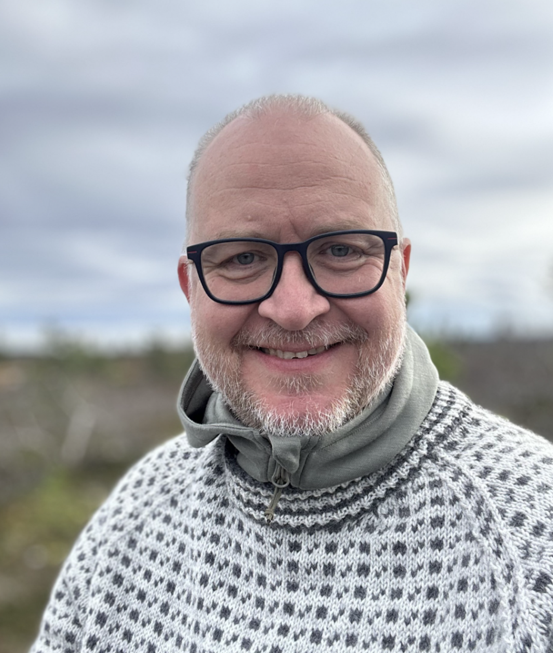 a man wearing glasses and a sweater smiles for the camera