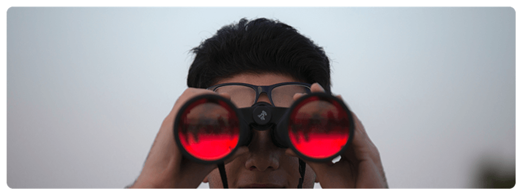 A photo of a man looking straight at the camera with a set of large binoculars.