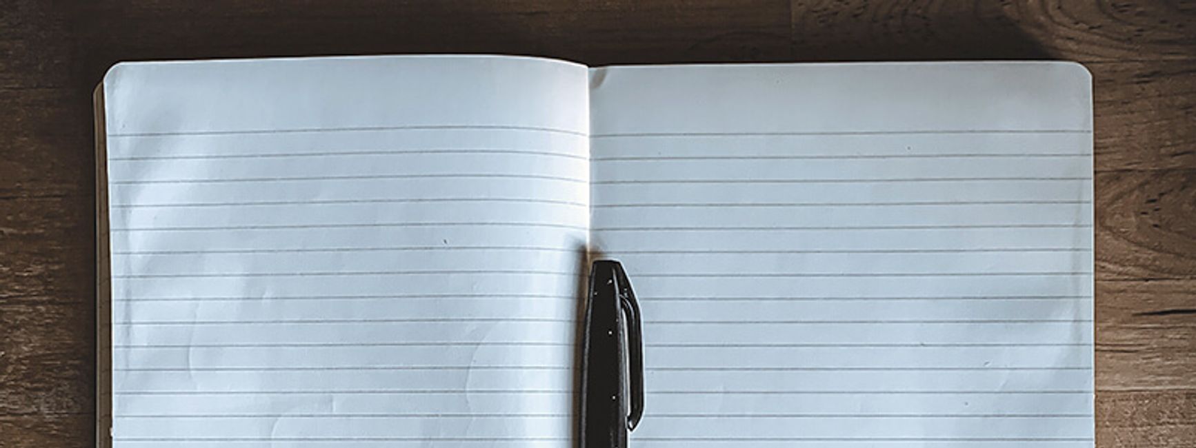 A photograph of a blank notebook open with a pen resting on the spine.