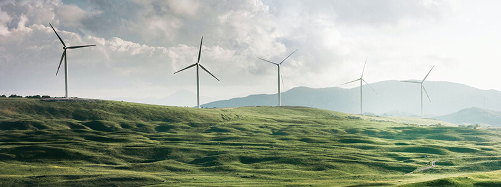 A photo of a green hill with large wind turbines collecting images.