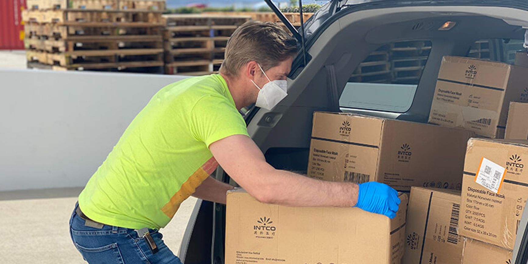 A photo of a man loading up cardboard boxes into the back of a van.