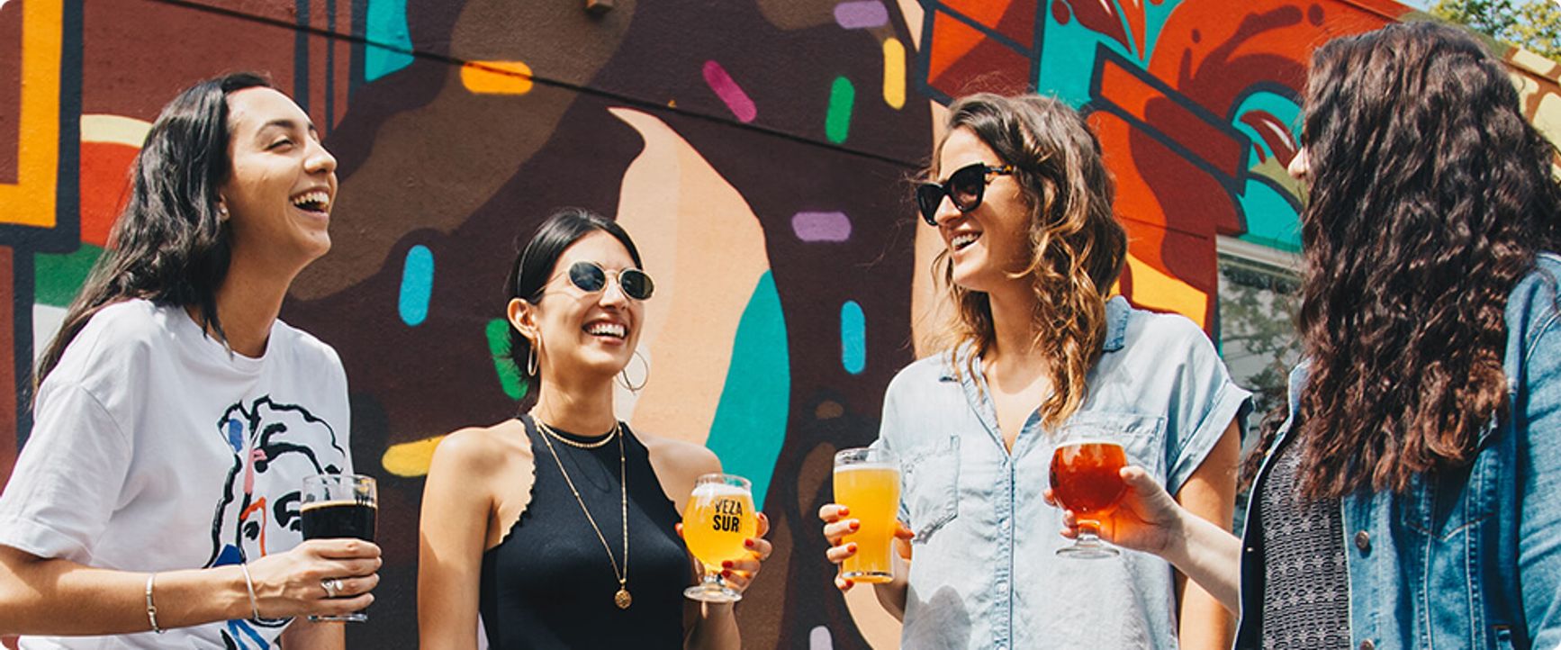 Four women laughing together, holding drinks.