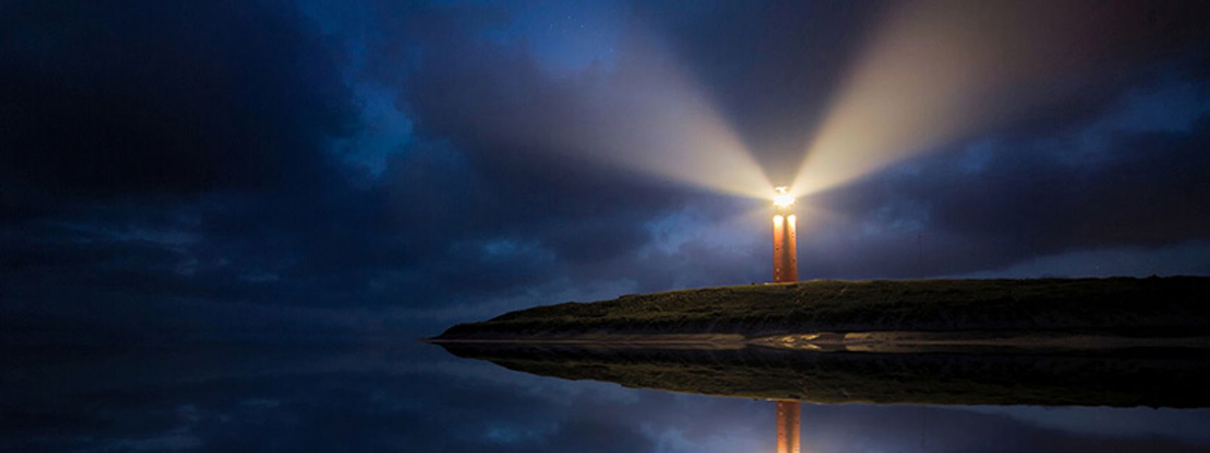 A photo of lighthouse at night, with lightbeams visible through the fog.