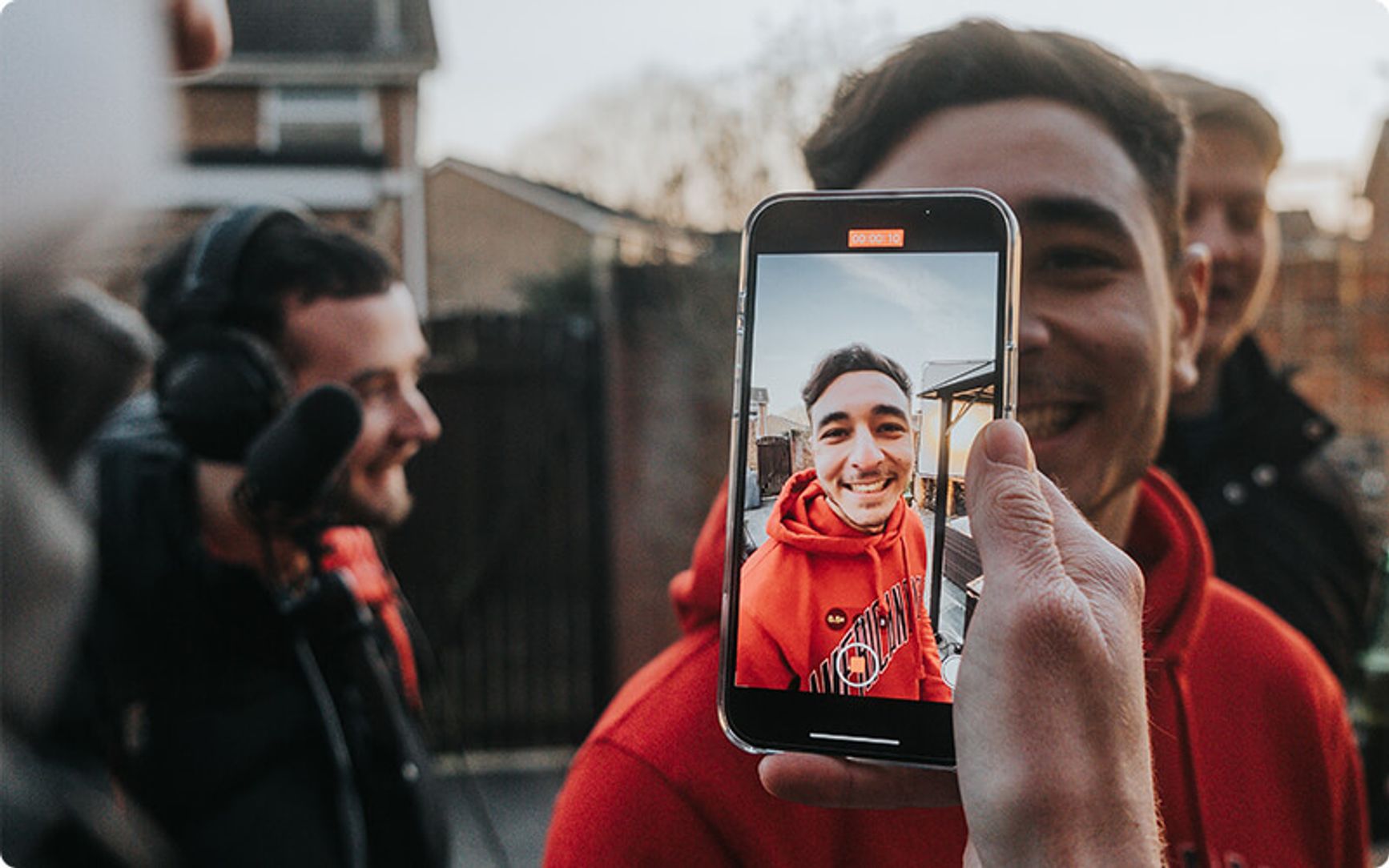A photo of a small production crew filming an influencer with a cell phone.